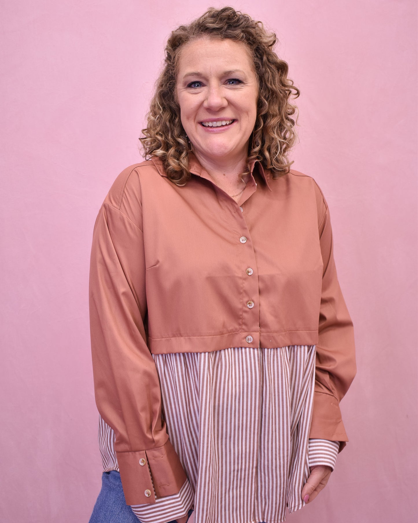 Woman wearing a peach-colored shirt over a striped dress against a pink background