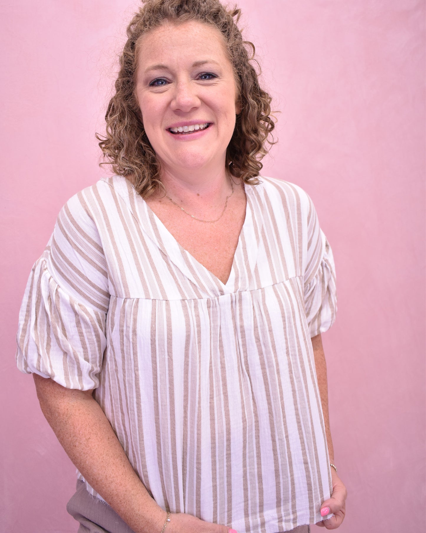 Woman wearing a white and beige striped shirt against a pink background