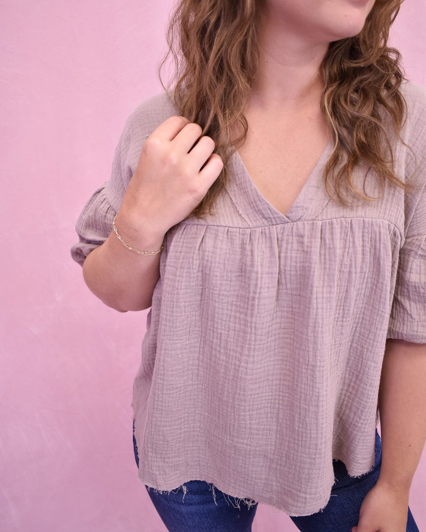 Person wearing a light purple blouse with a pink background