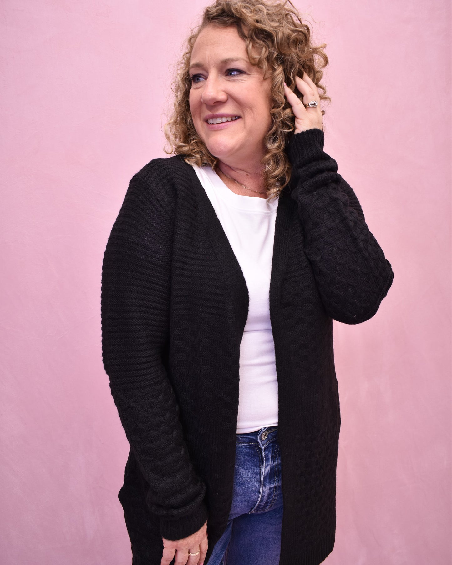 Woman wearing a black cardigan over a white shirt with a pink background