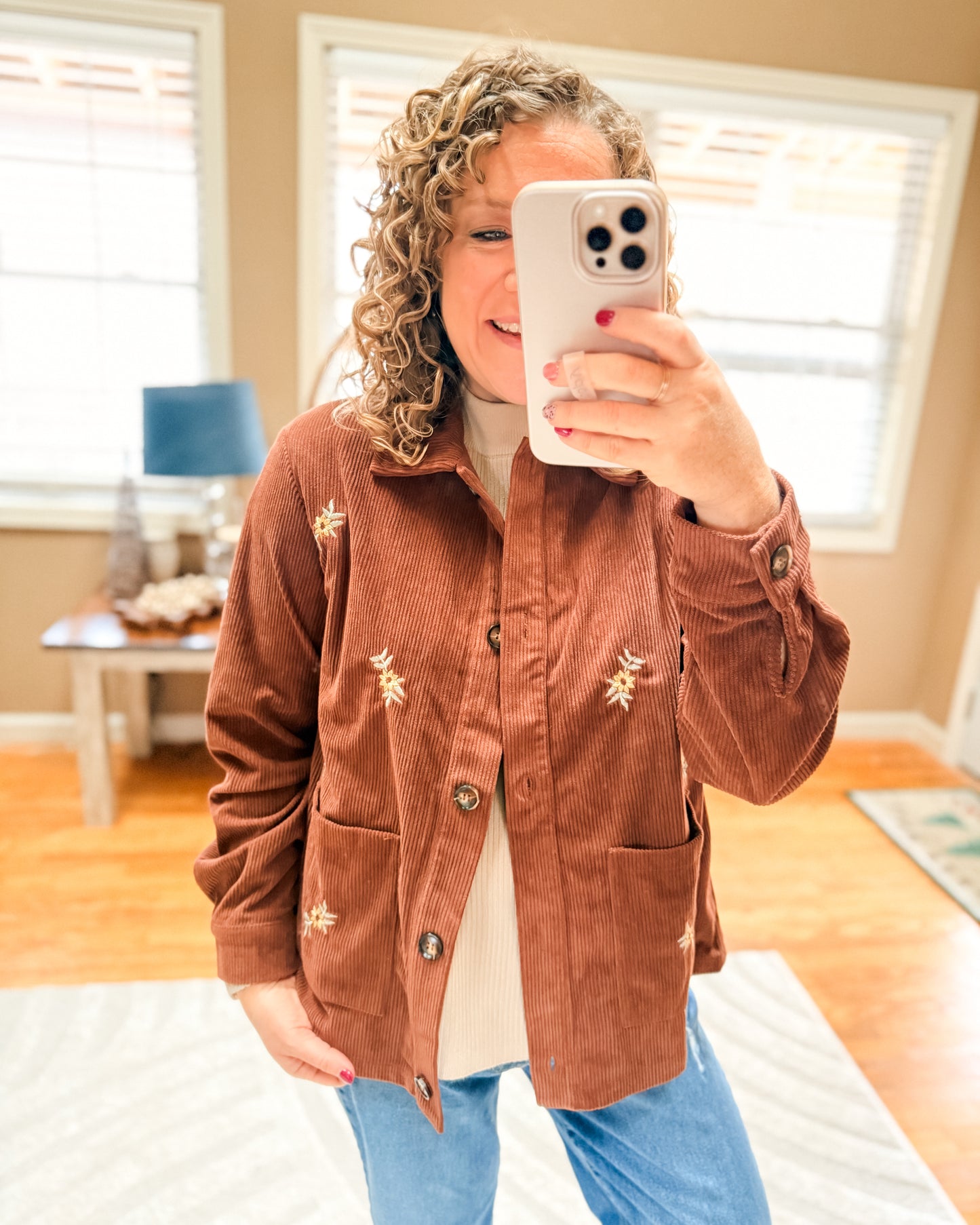 Person wearing a brown jacket with star patterns, taking a mirror selfie in a room.