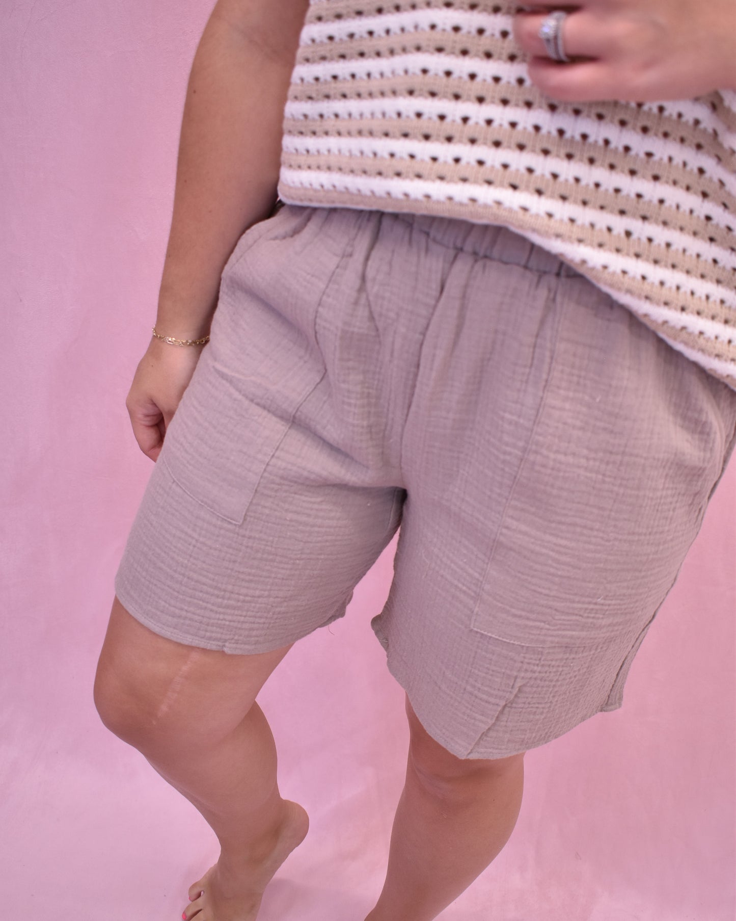 Person wearing light purple shorts and a striped shirt on a pink background