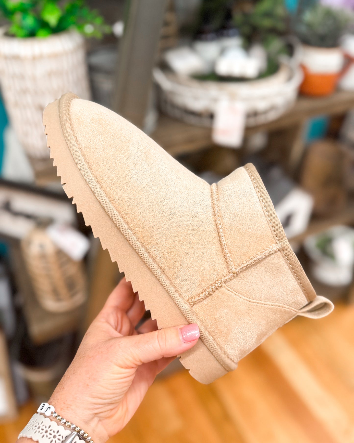 Beige suede shoe held by a hand with a blurred indoor background