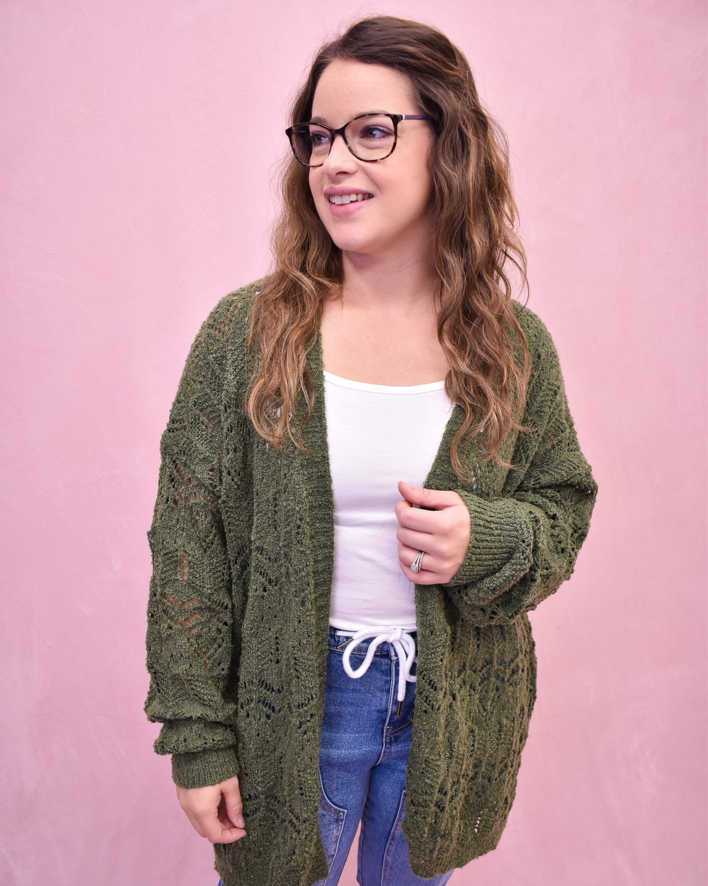 Woman wearing a green knitted cardigan over a white shirt with a pink background