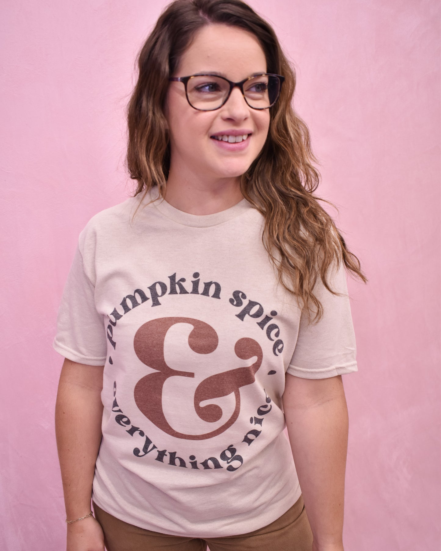 Person wearing a 'Pumpkin spice & everything nice' t-shirt against a pink background