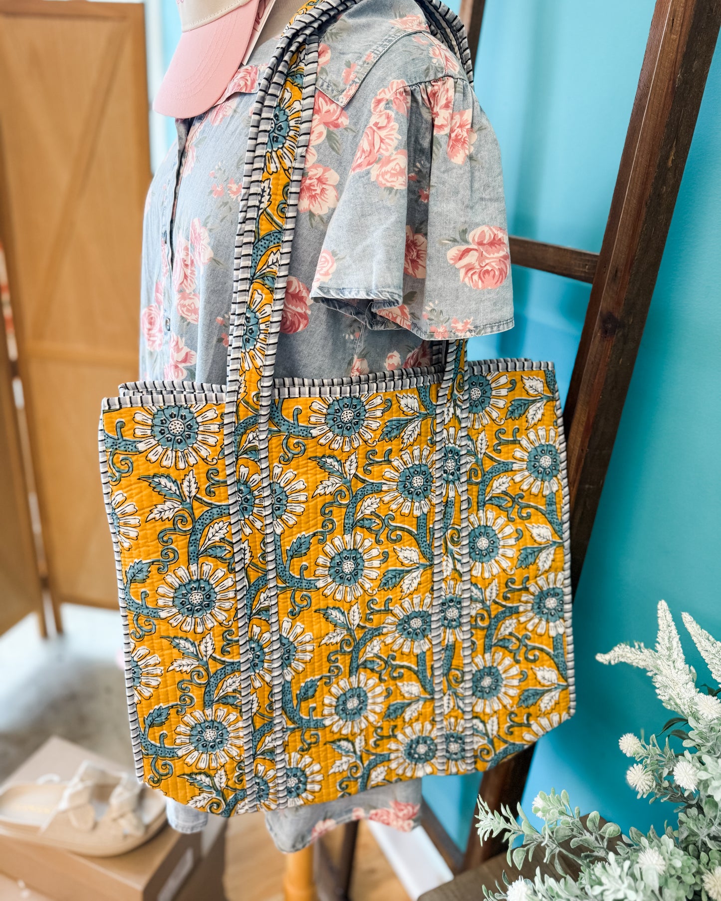 Floral-patterned bag with a yellow and blue design held by a person against a blue wall.