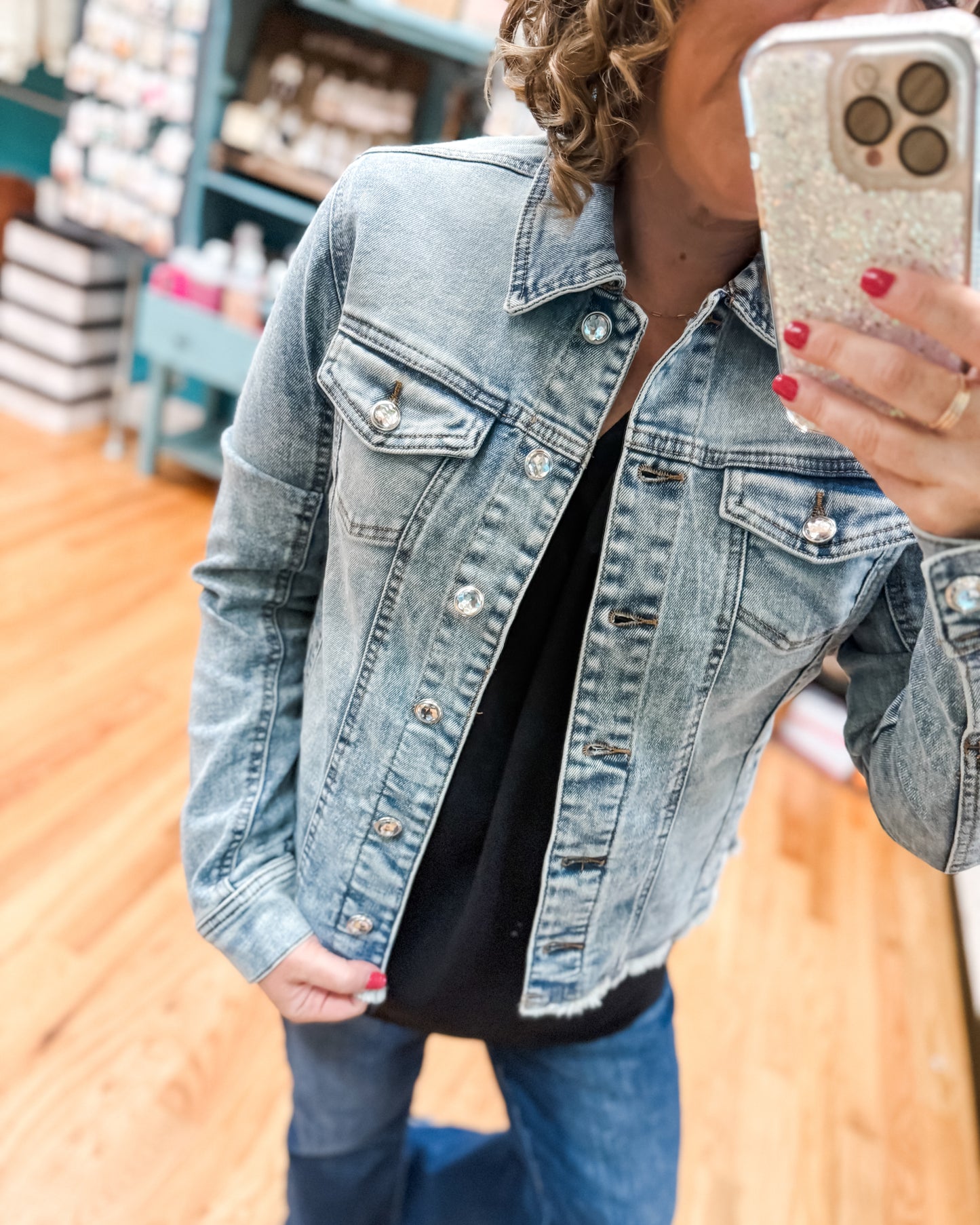 Person wearing a denim jacket taking a selfie with a phone.