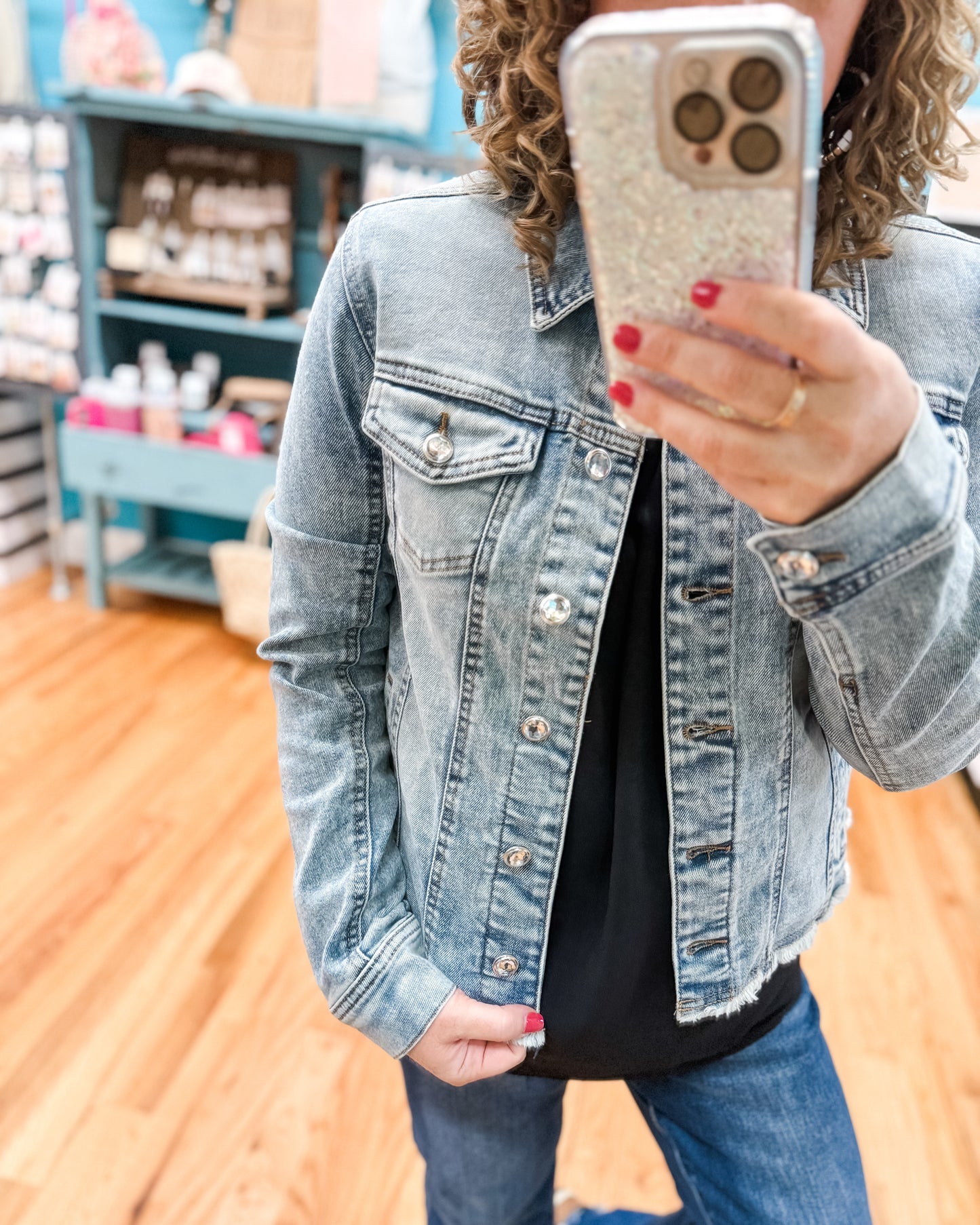 Person wearing a denim jacket taking a mirror selfie in a store.