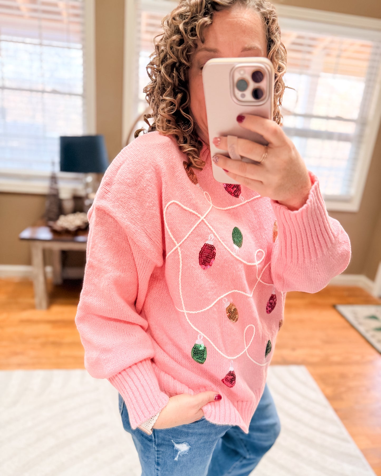Person wearing a pink sweater with colorful designs, taking a mirror selfie.