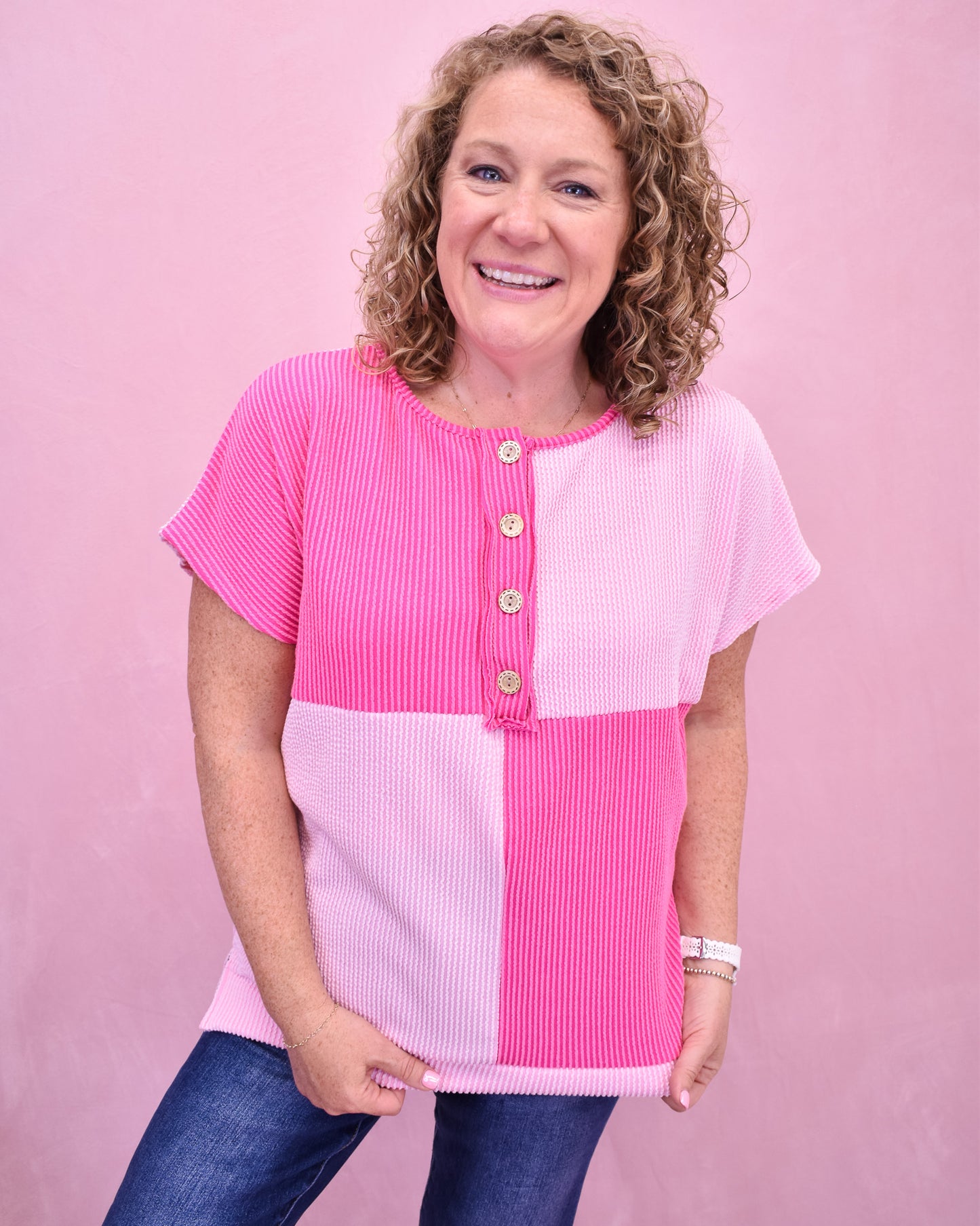 Woman wearing a pink and white color-blocked top against a pink background