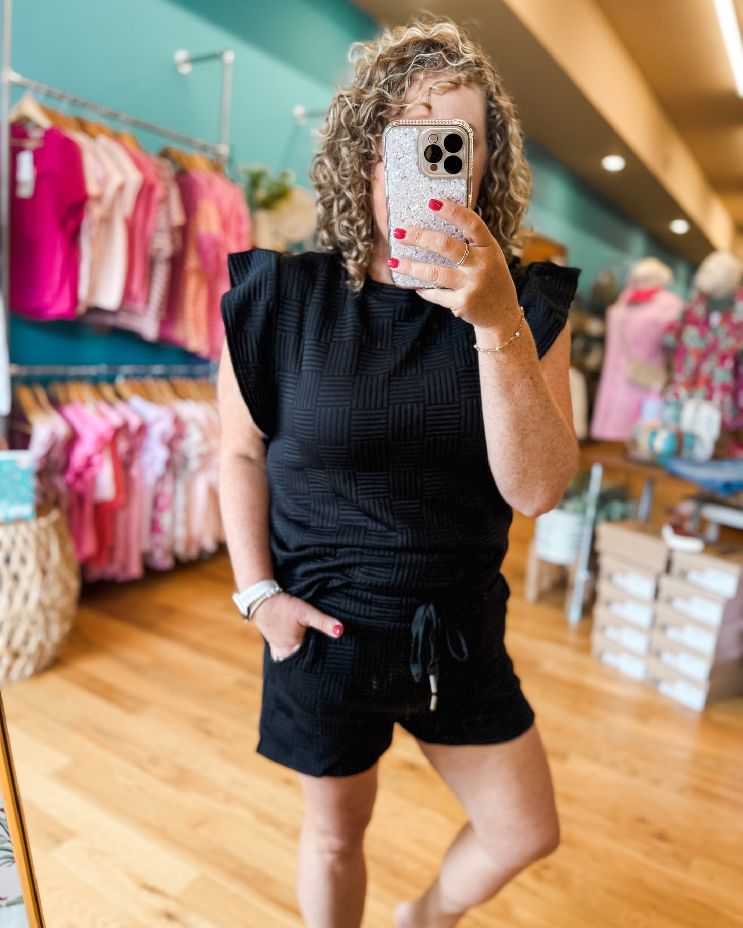 Woman taking a mirror selfie wearing a black outfit in a store.