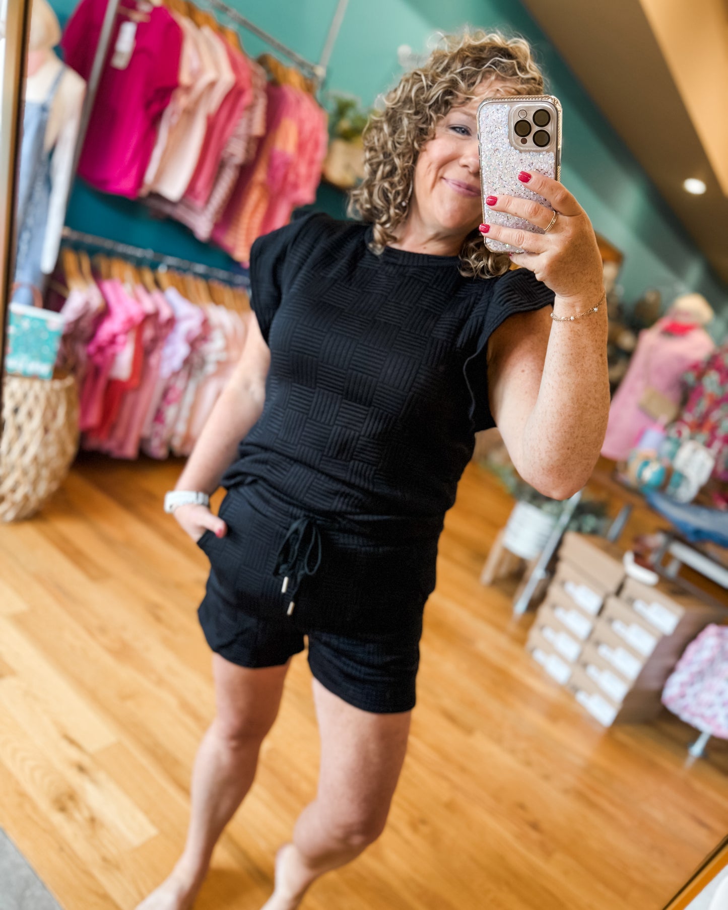 Woman taking a mirror selfie in a store wearing a black outfit.