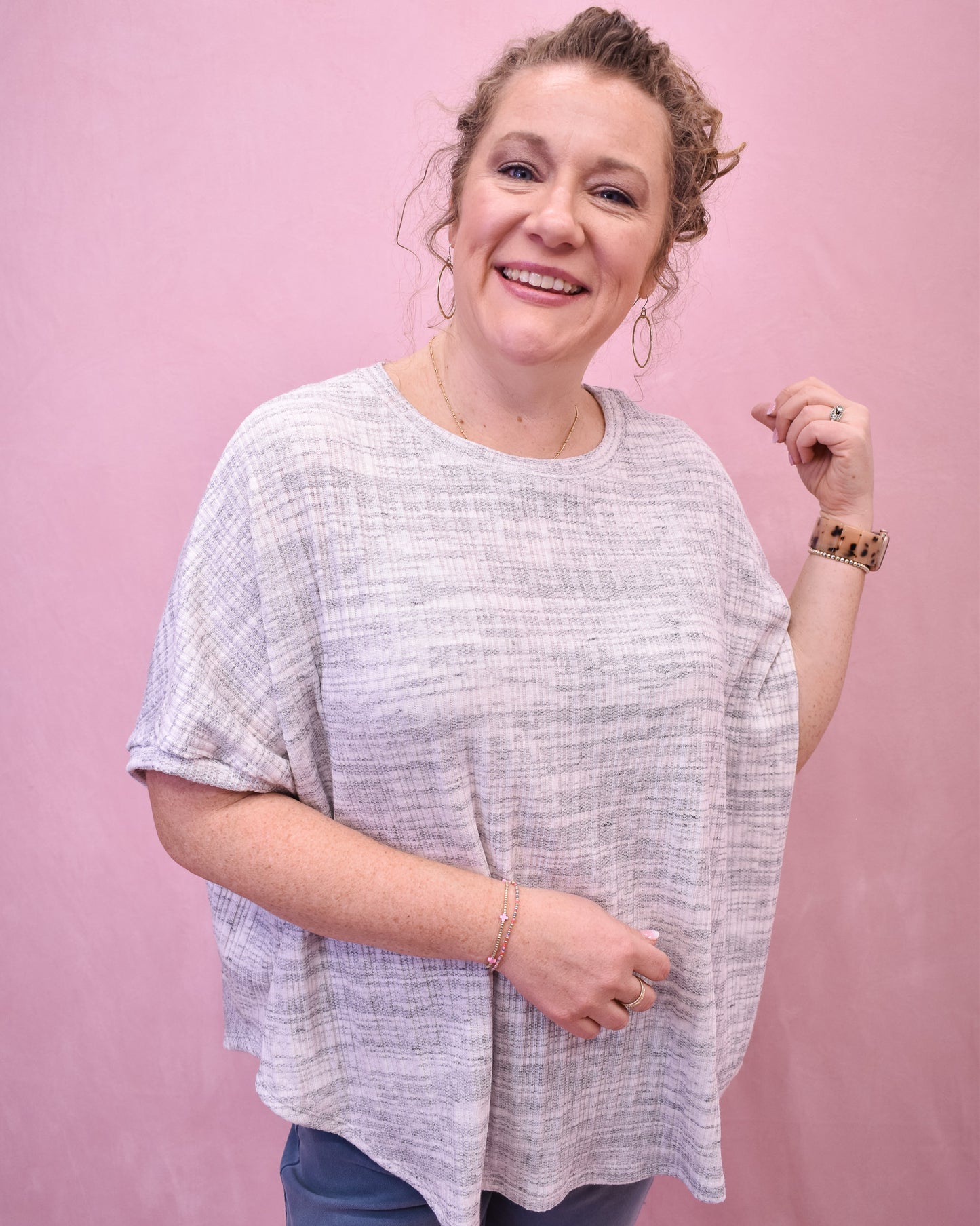 Woman wearing a light gray oversized shirt against a pink background