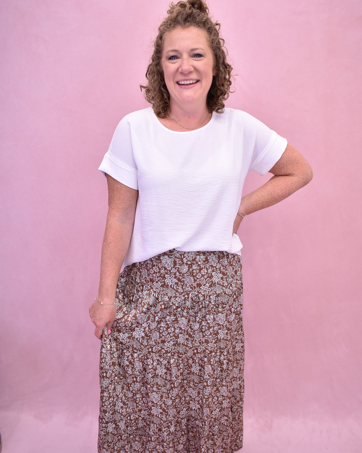 Woman wearing a white t-shirt and floral skirt against a pink background