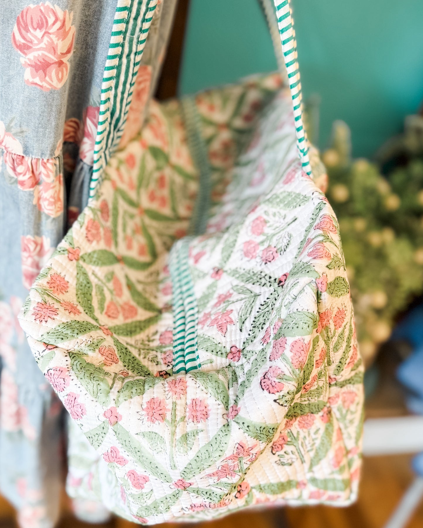 Floral-patterned bag with green straps hanging on a rack against a blurred background