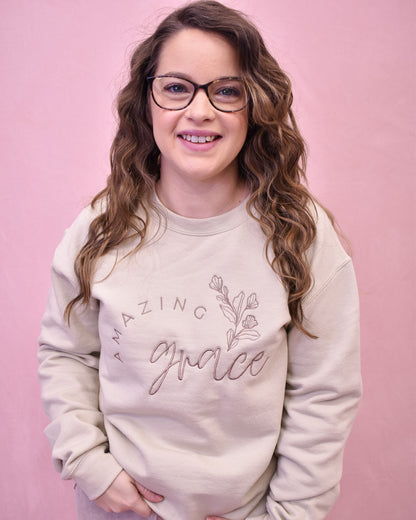 Person wearing a beige sweatshirt with 'Amazing Grace' text on a pink background