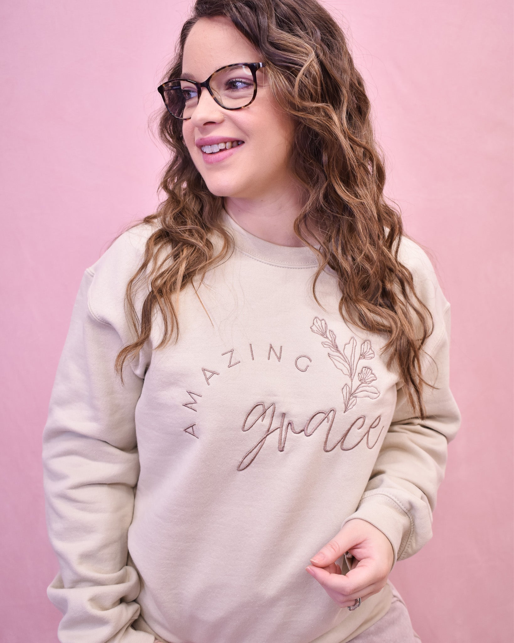 Person wearing a beige sweatshirt with 'Amazing Grace' text on a pink background