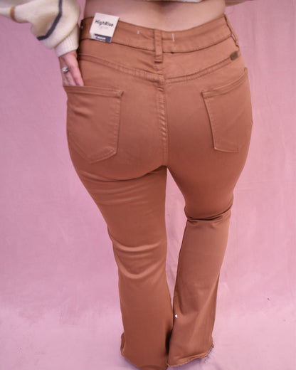 Brown flared pants worn by a person on a pink background