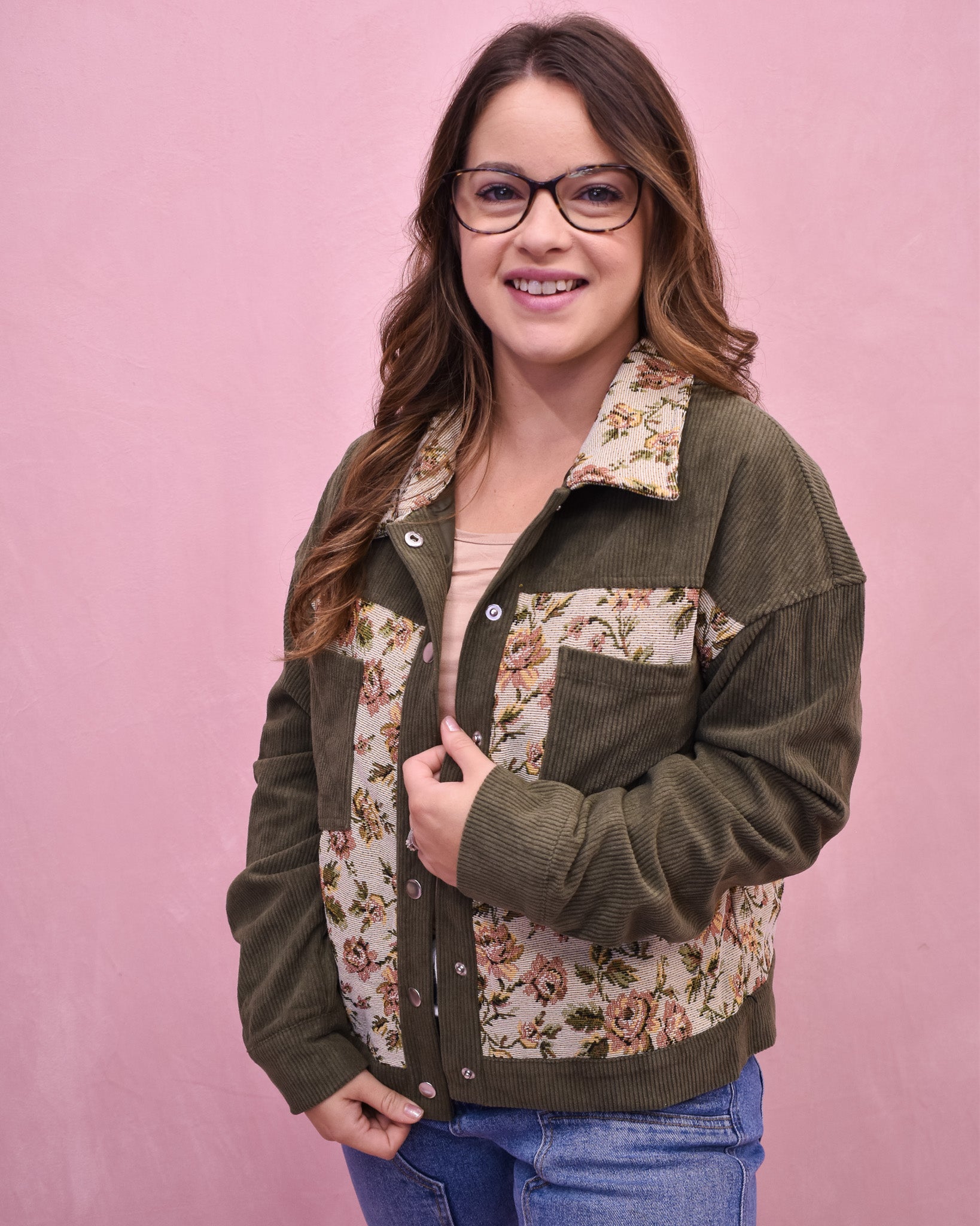 Woman wearing a green jacket with floral patterns on a pink background