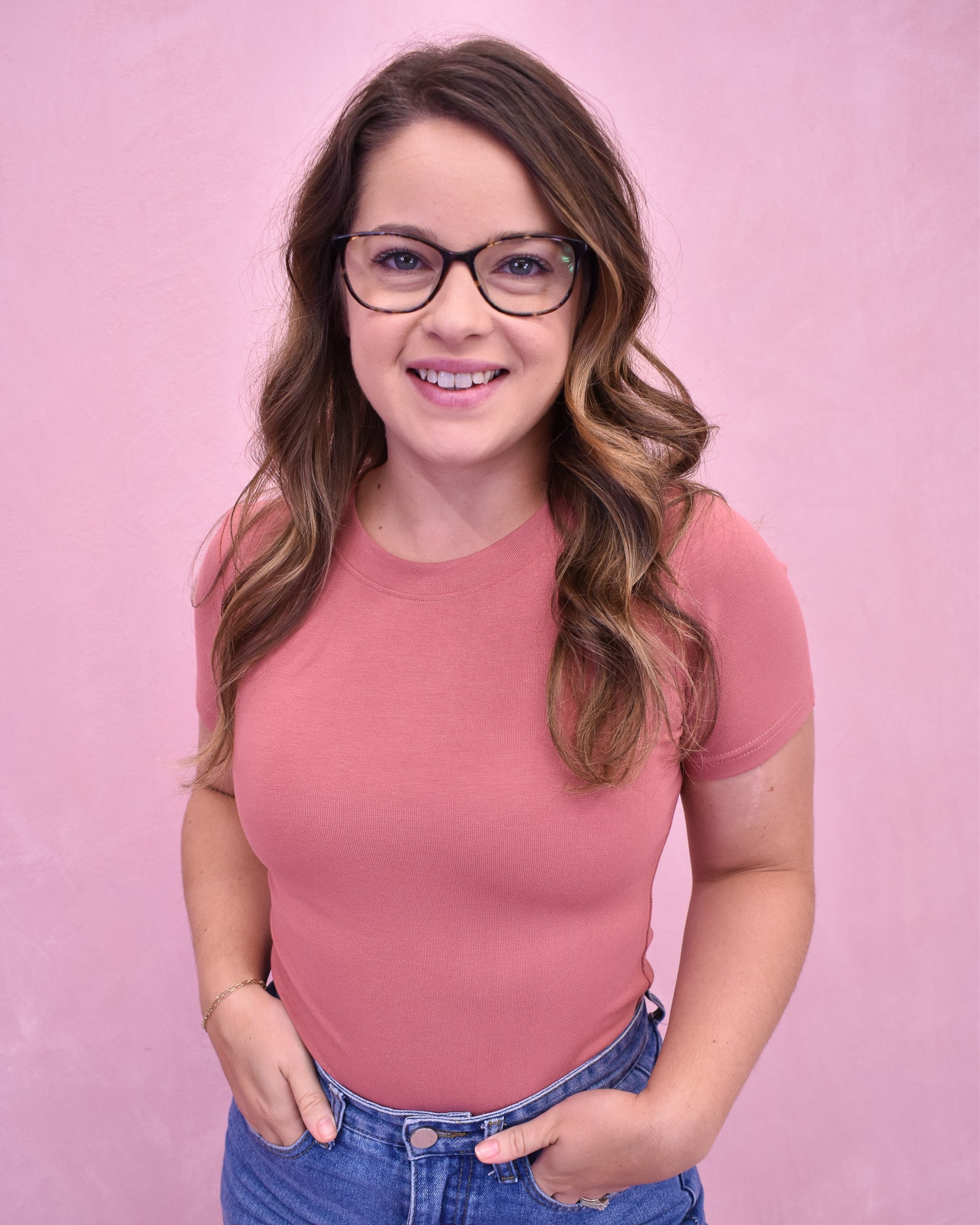 Woman wearing a pink top and blue jeans against a pink background