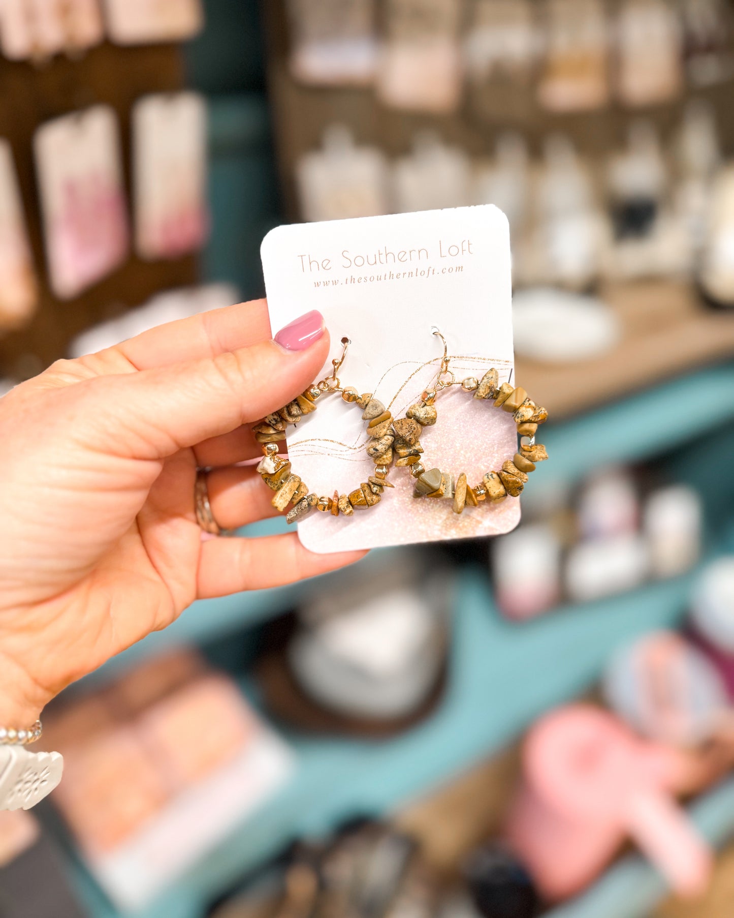 Hand holding a pair of earrings on a branded card with a blurred store background