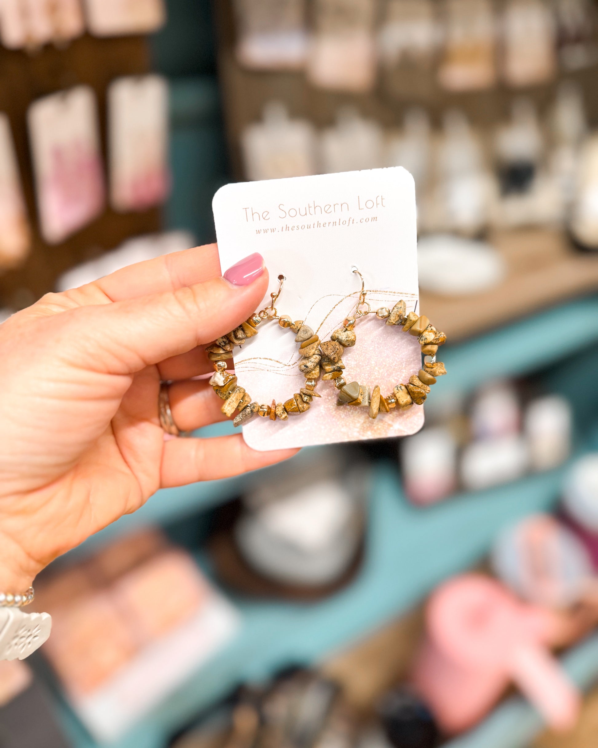 Hand holding a pair of earrings on a branded card with a blurred store background