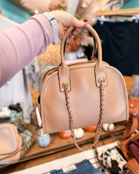 Beige handbag with a chain detail held by a person in a store setting.