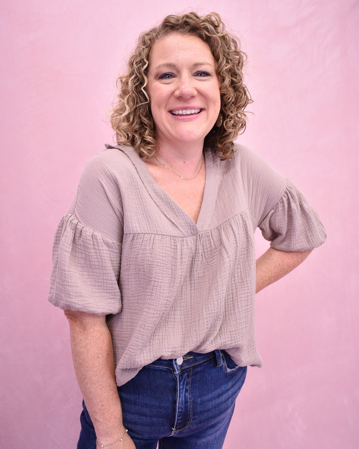 Woman wearing a light purple blouse with ruffled sleeves against a pink background