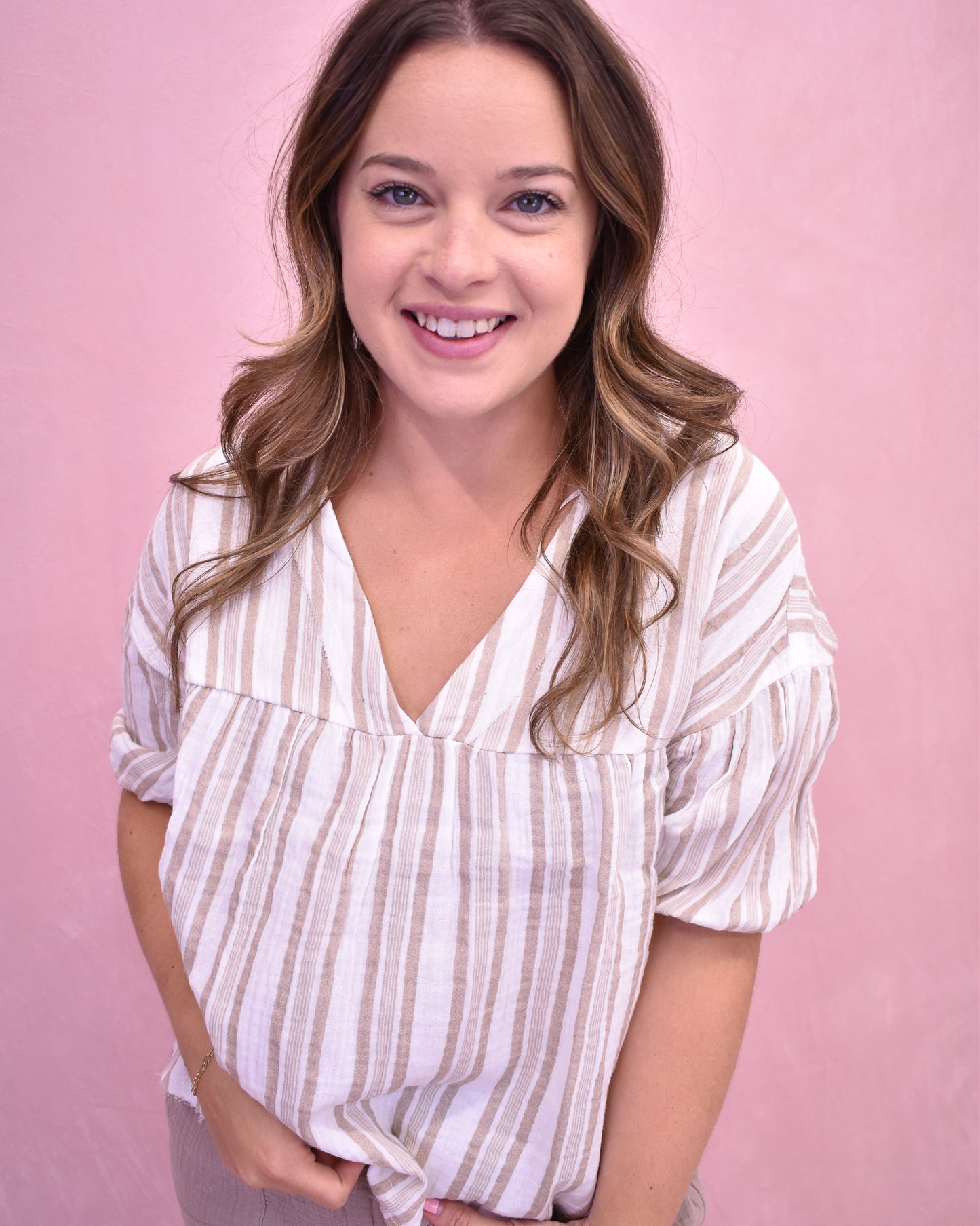 Woman wearing a white and beige striped shirt against a pink background