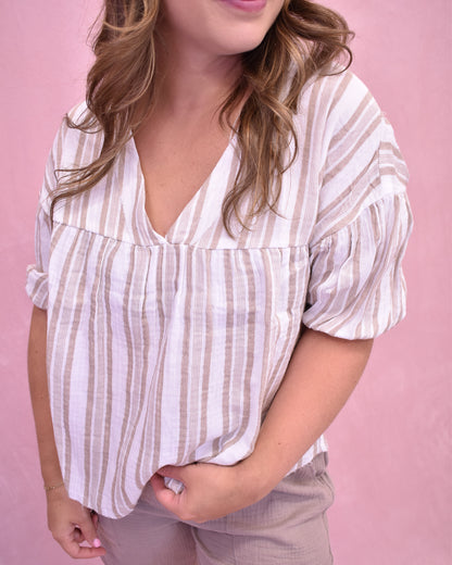 Woman wearing a white and beige striped blouse against a pink background