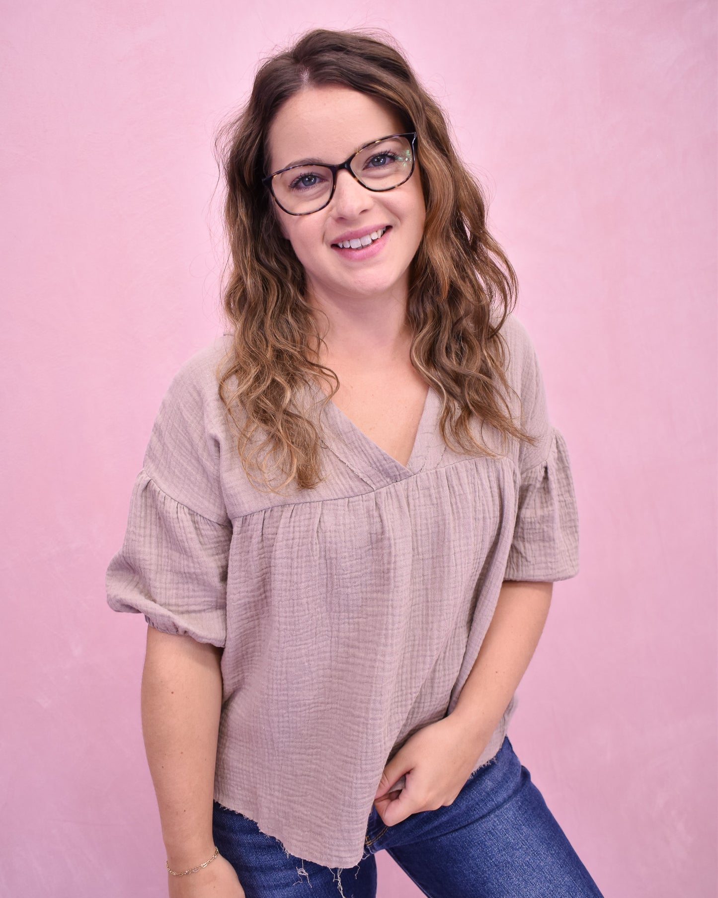 Woman wearing a light purple blouse and blue jeans against a pink background