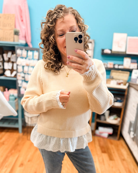 Woman taking a mirror selfie wearing a beige sweater with lace trim in a store.