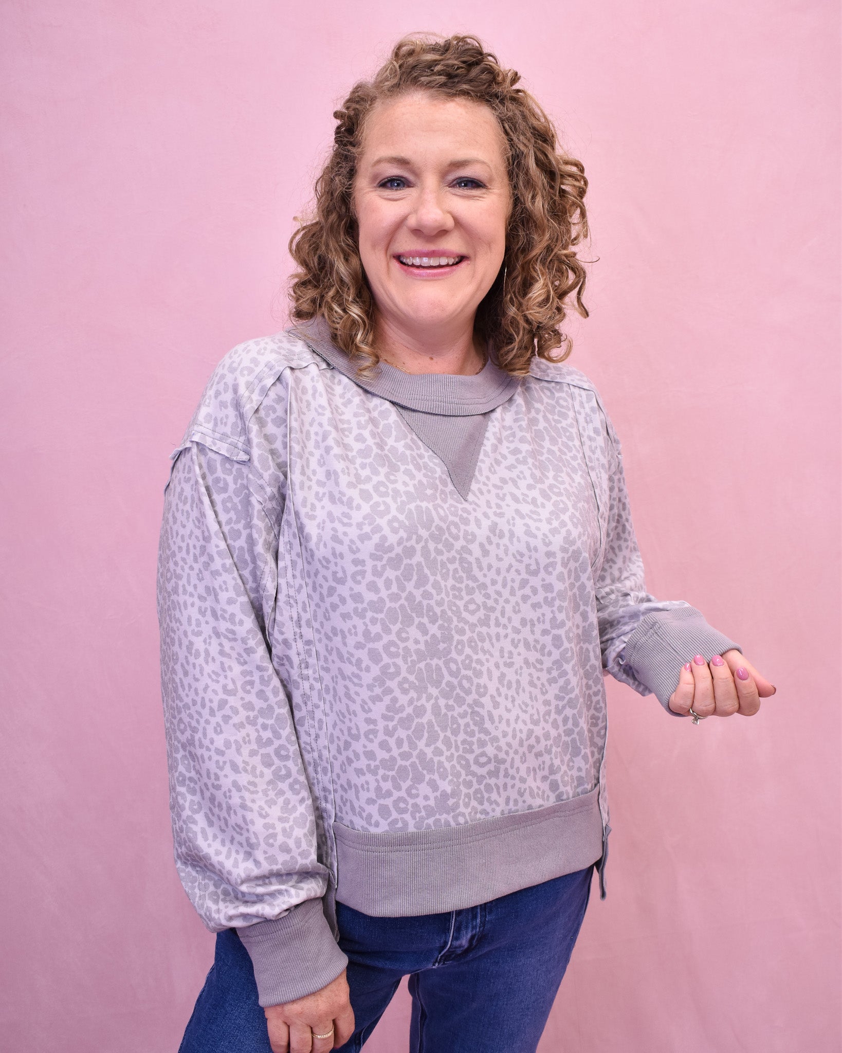 Woman wearing a light gray patterned sweatshirt against a pink background
