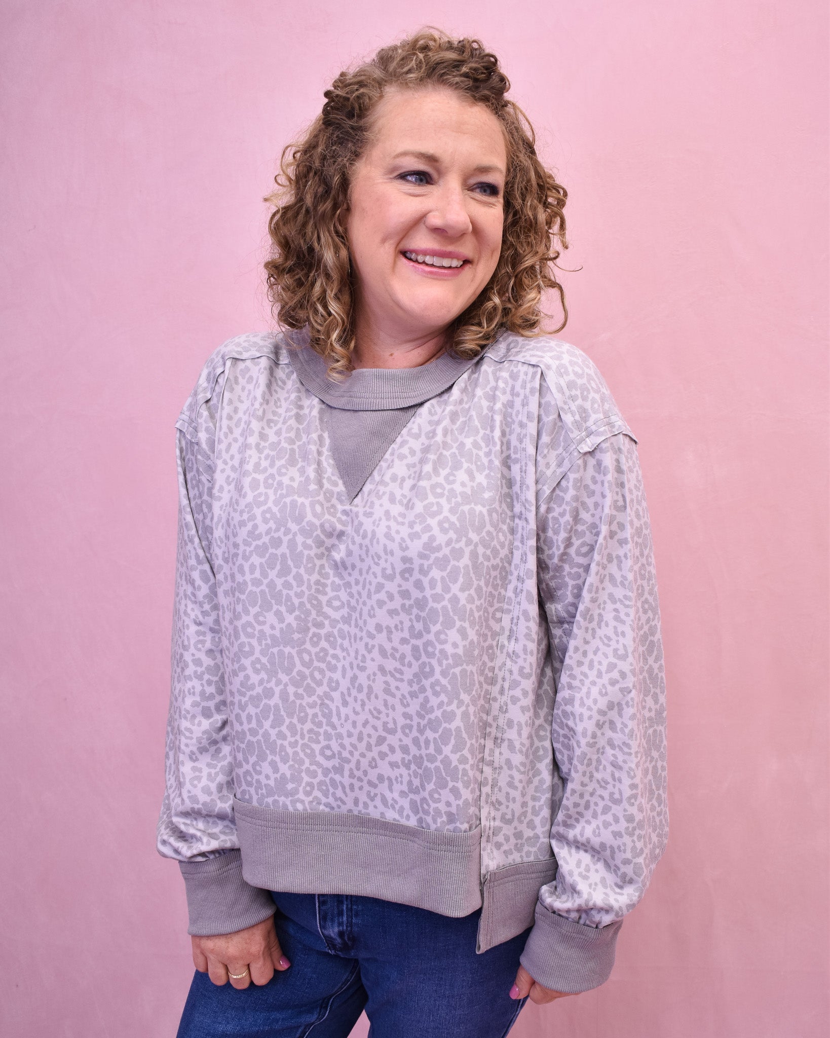 Person wearing a light gray patterned sweater with a pink background