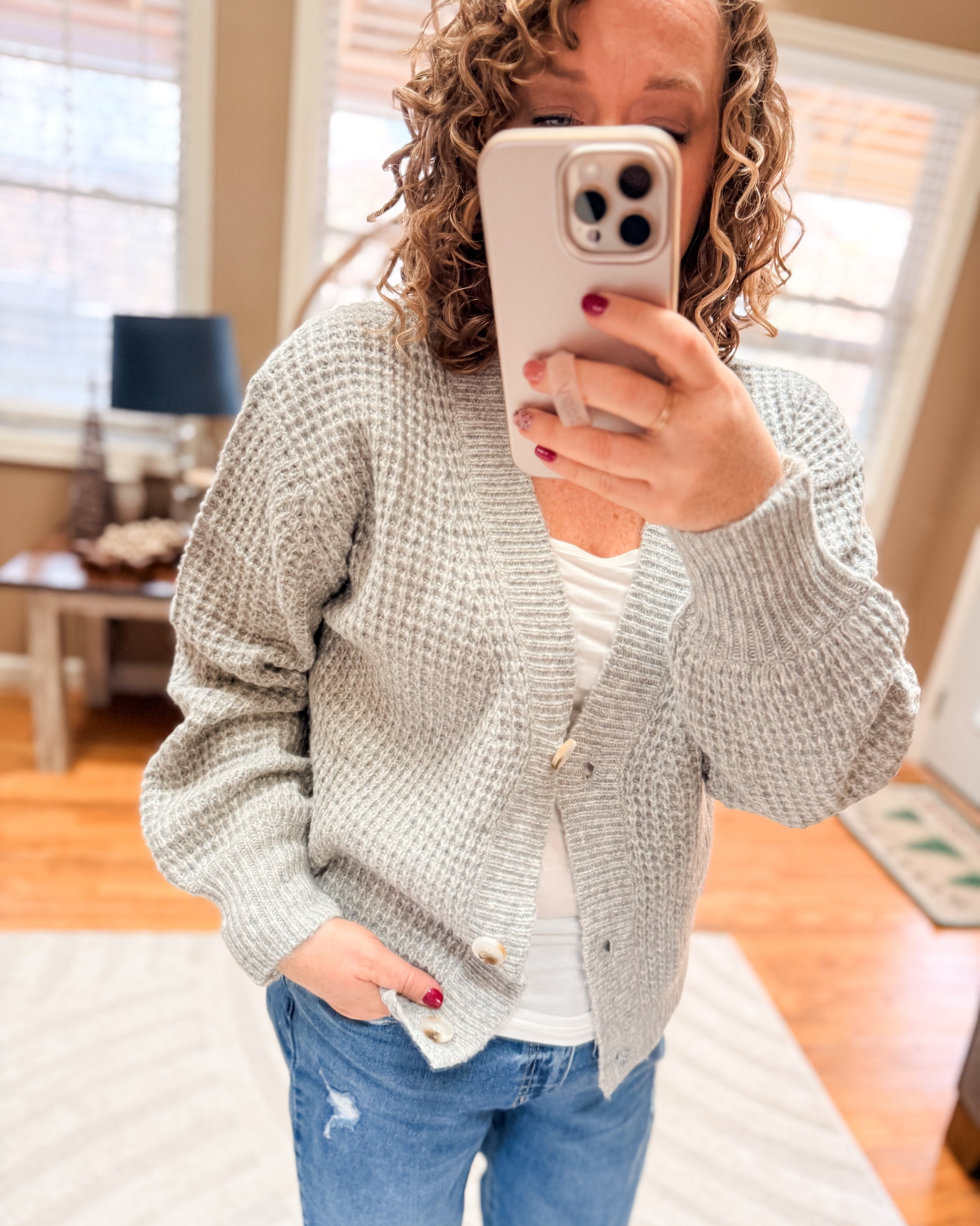 Person wearing a gray textured sweater and blue jeans, taking a mirror selfie.