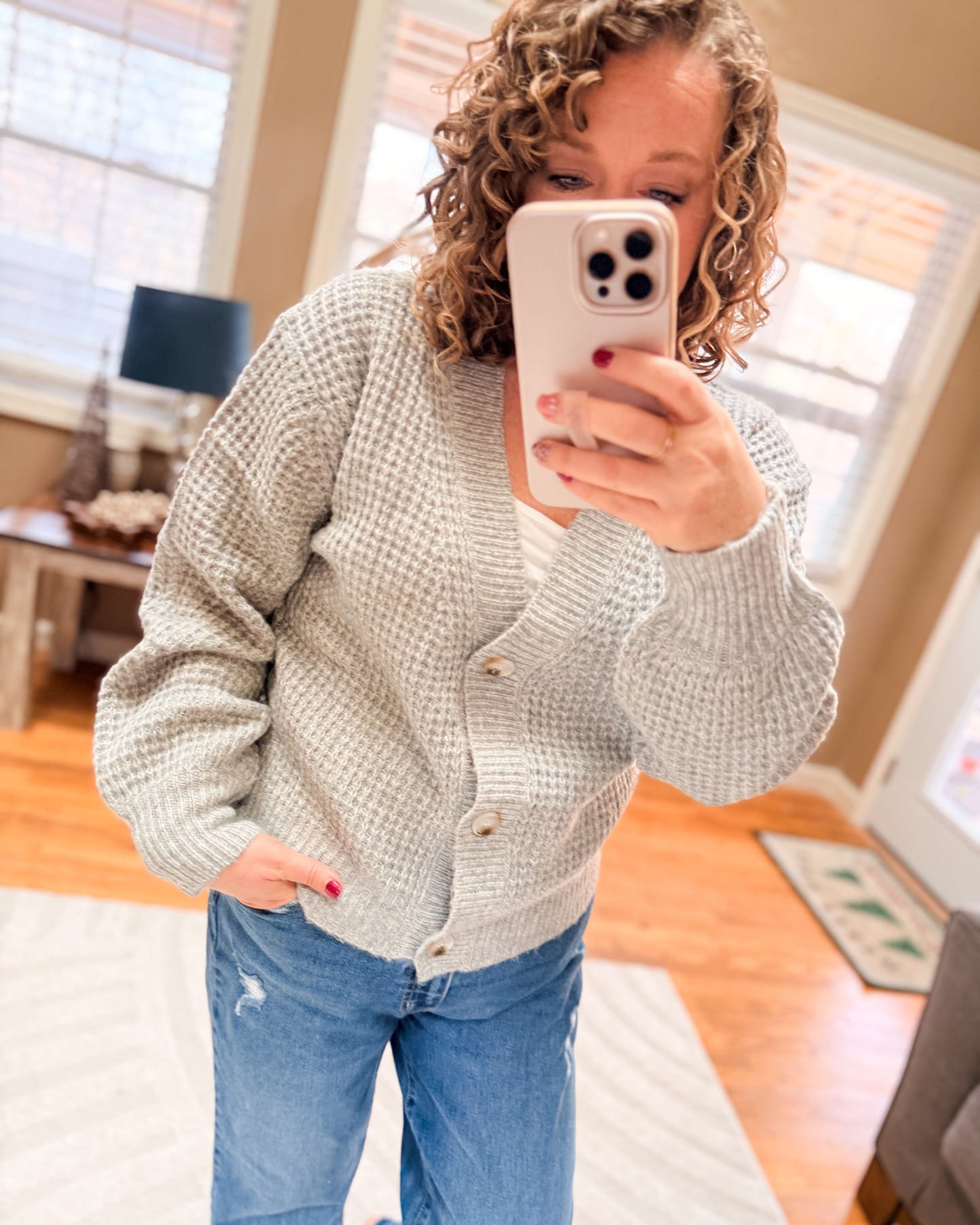 Person wearing a light gray textured sweater and blue jeans taking a mirror selfie.