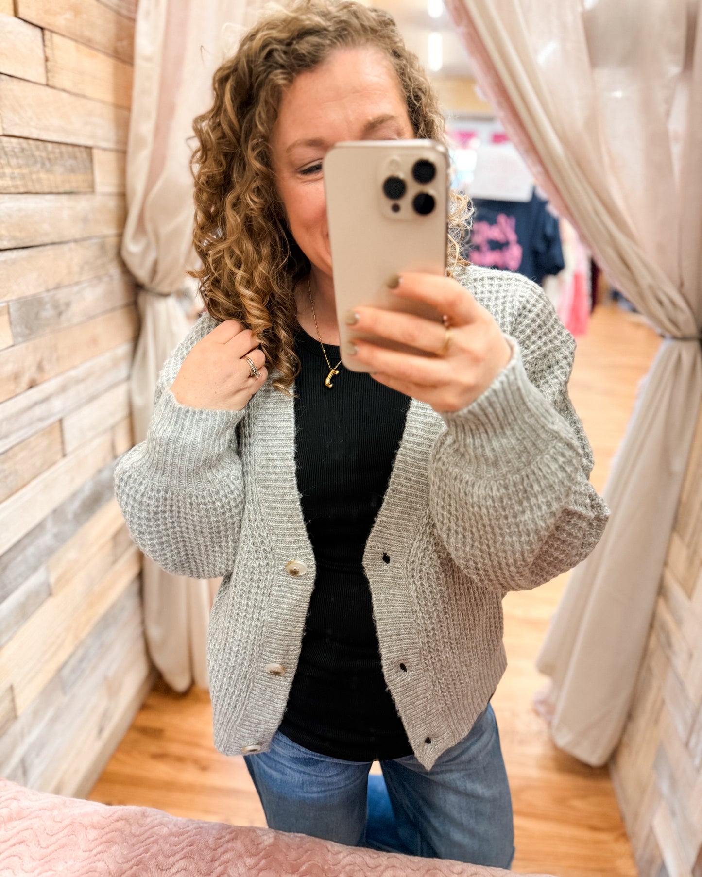 Person wearing a gray cardigan taking a mirror selfie in a store.