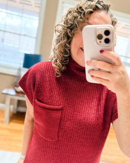 Person wearing a red sleeveless sweater taking a selfie indoors.