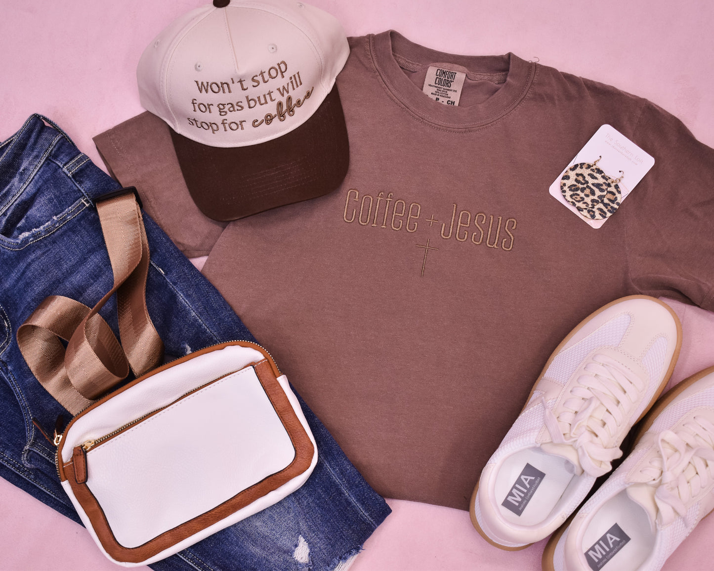 Brown t-shirt with 'Coffee + Jesus' text, cap, jeans, bag, and sneakers on a pink background