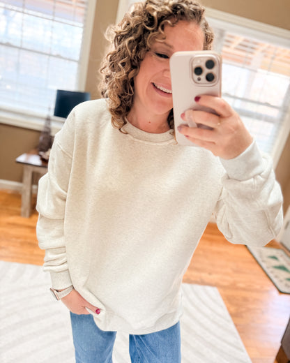 Woman taking a mirror selfie wearing a white sweater and blue jeans in a home setting.