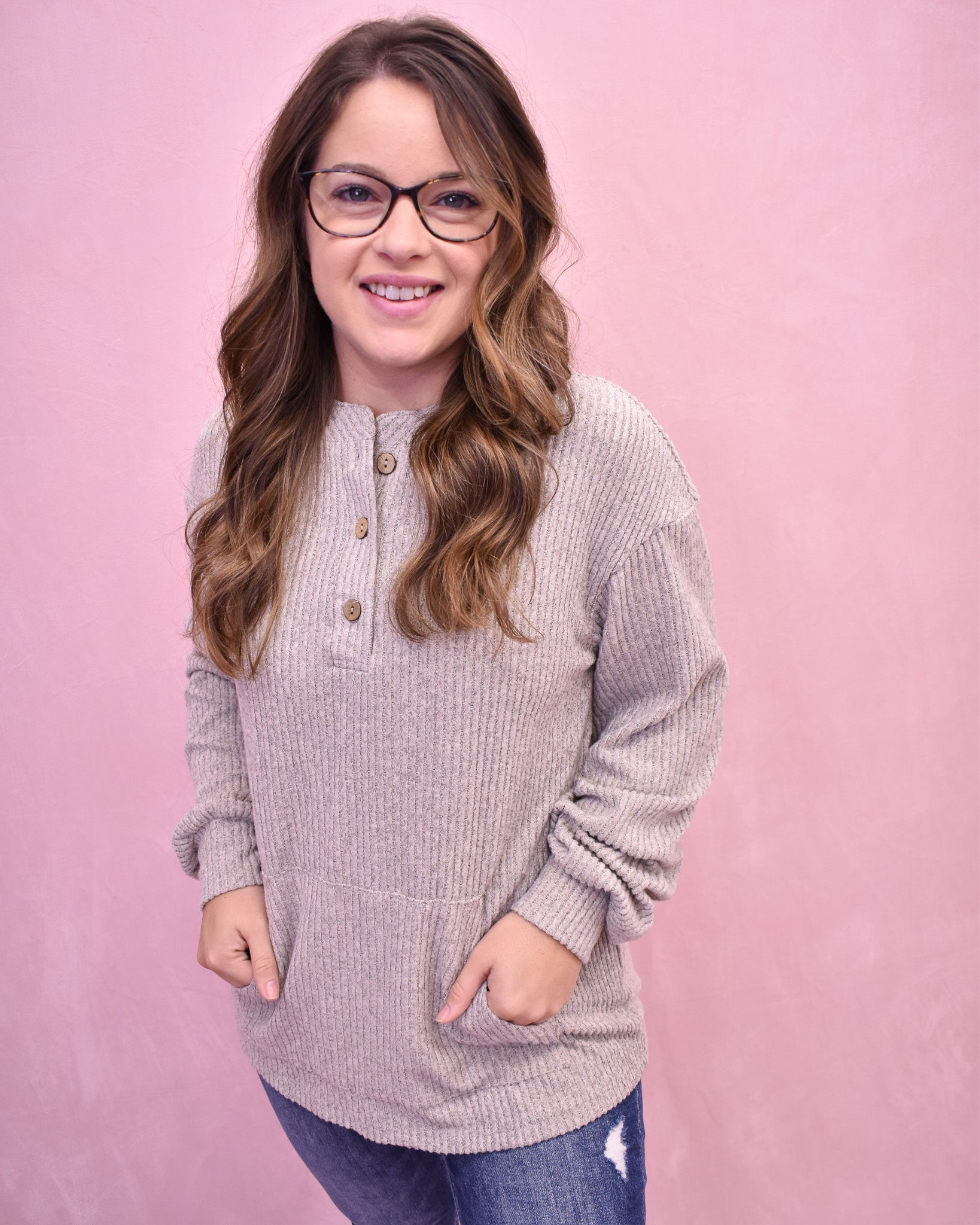 Woman wearing a light gray sweater with buttons against a pink background