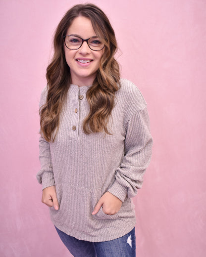 Woman wearing a light gray sweater with buttons against a pink background
