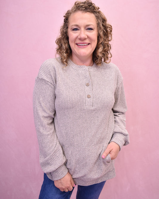 Woman wearing a light gray long-sleeve shirt against a pink background