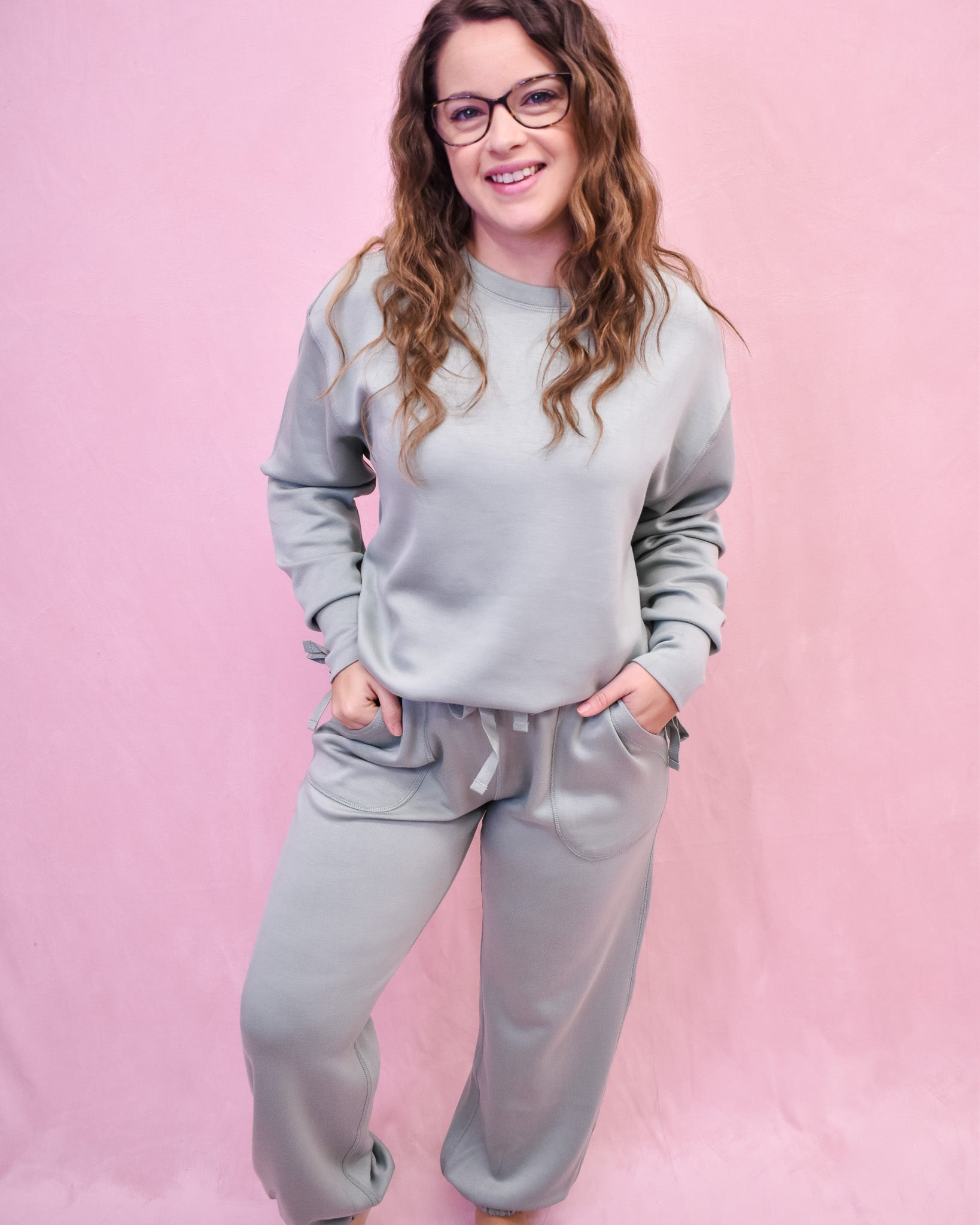 Woman wearing a gray sweatshirt and pants set against a pink background