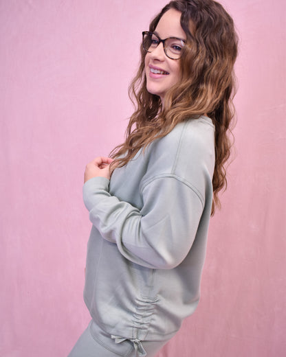 Woman wearing a light gray sweatshirt against a pink background