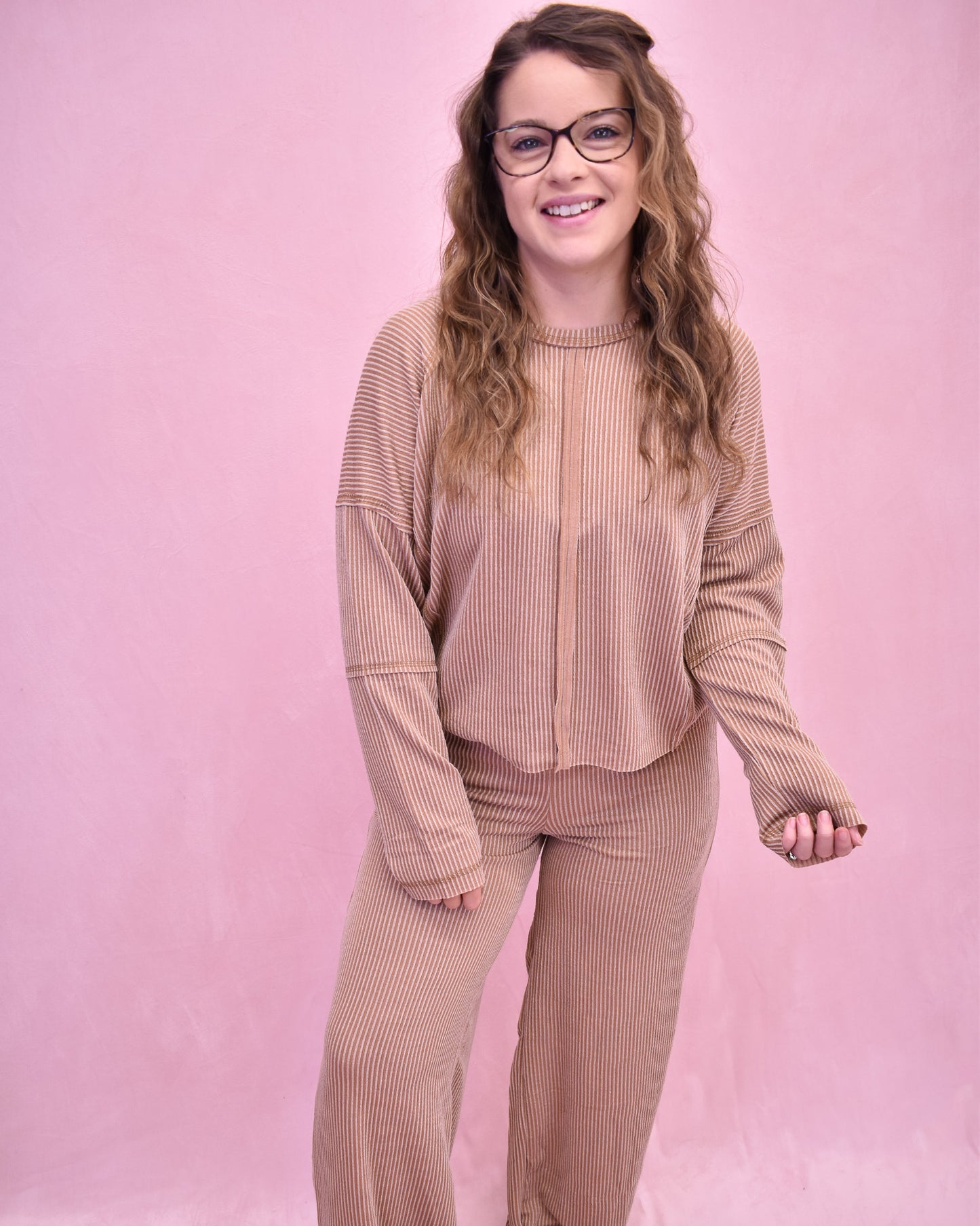 Woman wearing a beige ribbed outfit against a pink background