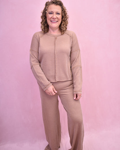 Woman wearing a beige ribbed lounge set against a pink background