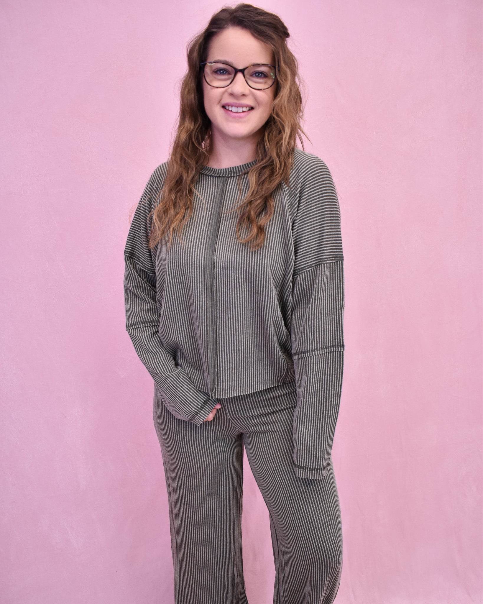 Woman wearing a gray ribbed sweater and pants against a pink background