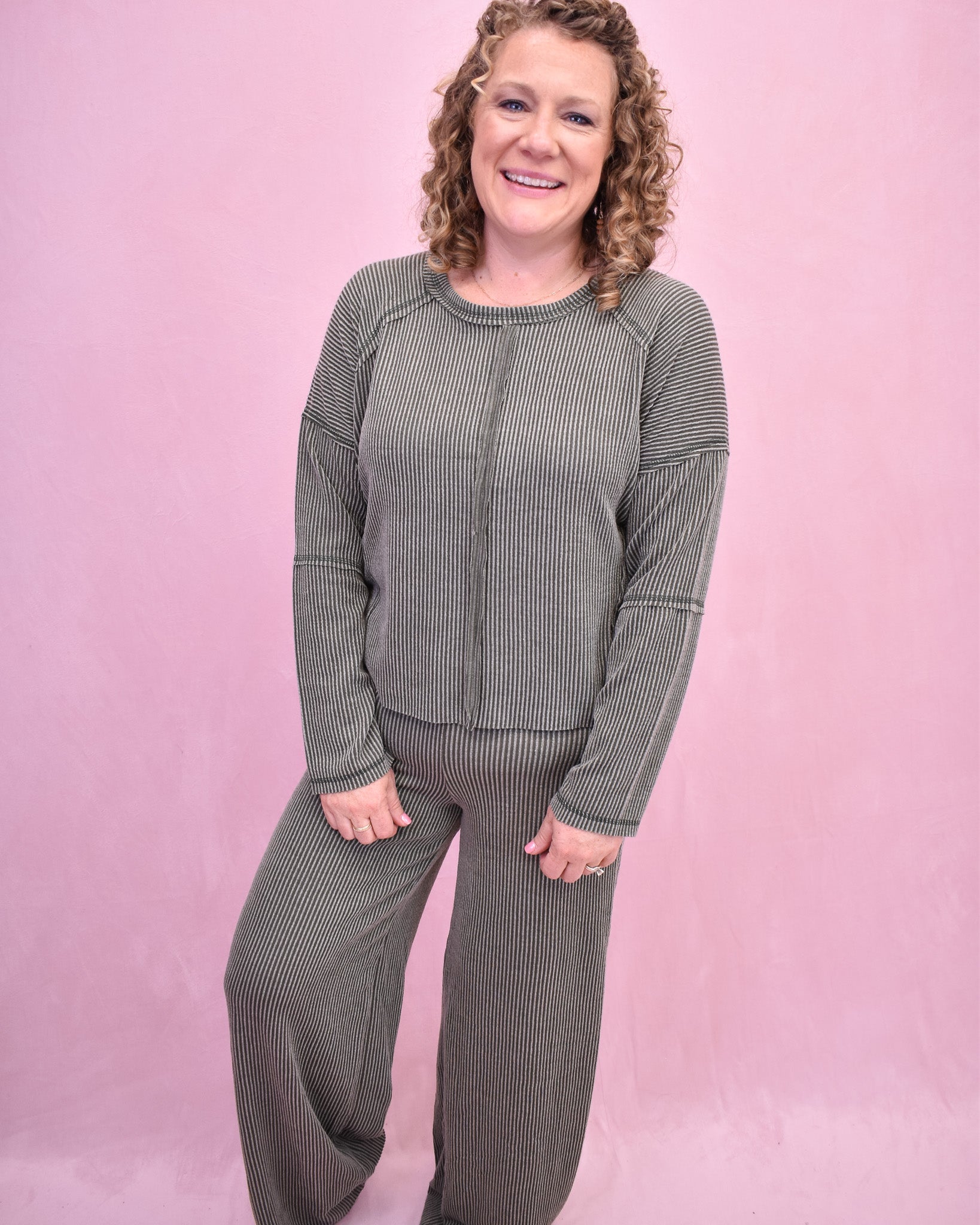 Woman wearing a green ribbed sweater and pants against a pink background