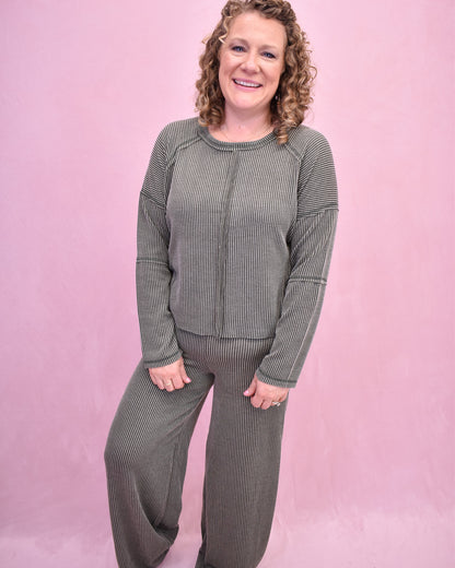 Woman wearing a green ribbed sweater and pants against a pink background